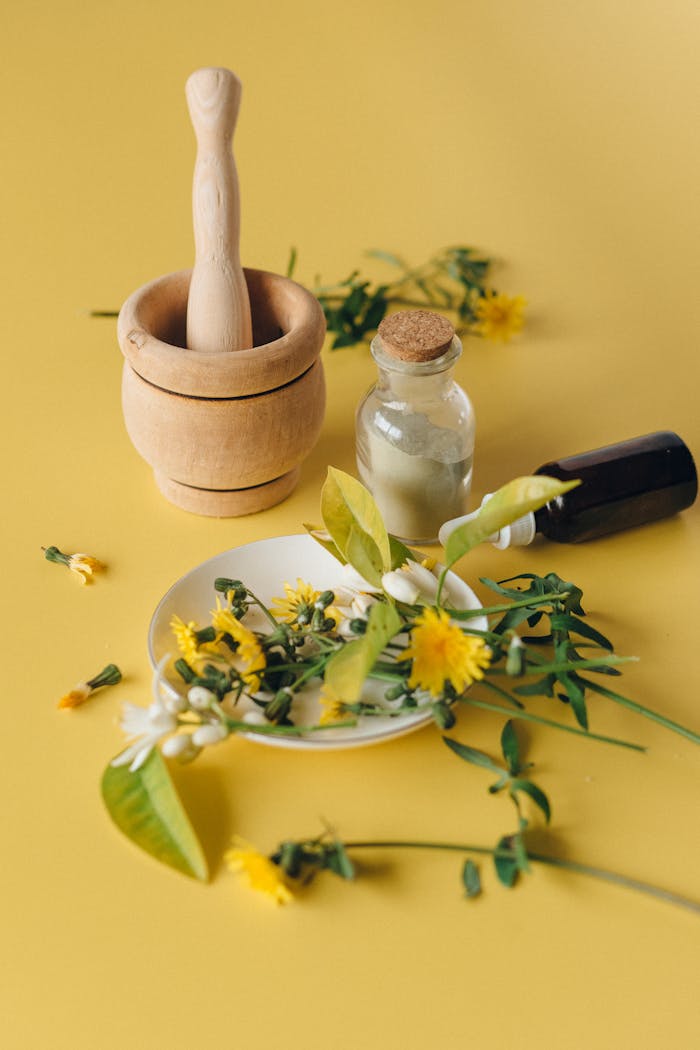 Ingredients for a natural herbal remedy with a mortar, pedestal, and bottle on a yellow surface.