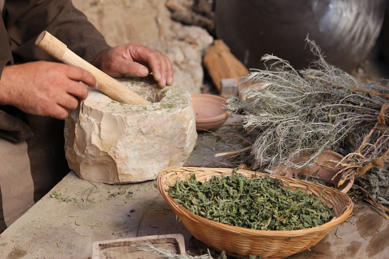 Hands grinding herbs in a rustic mortar and pestle setup, showcasing traditional preparation.